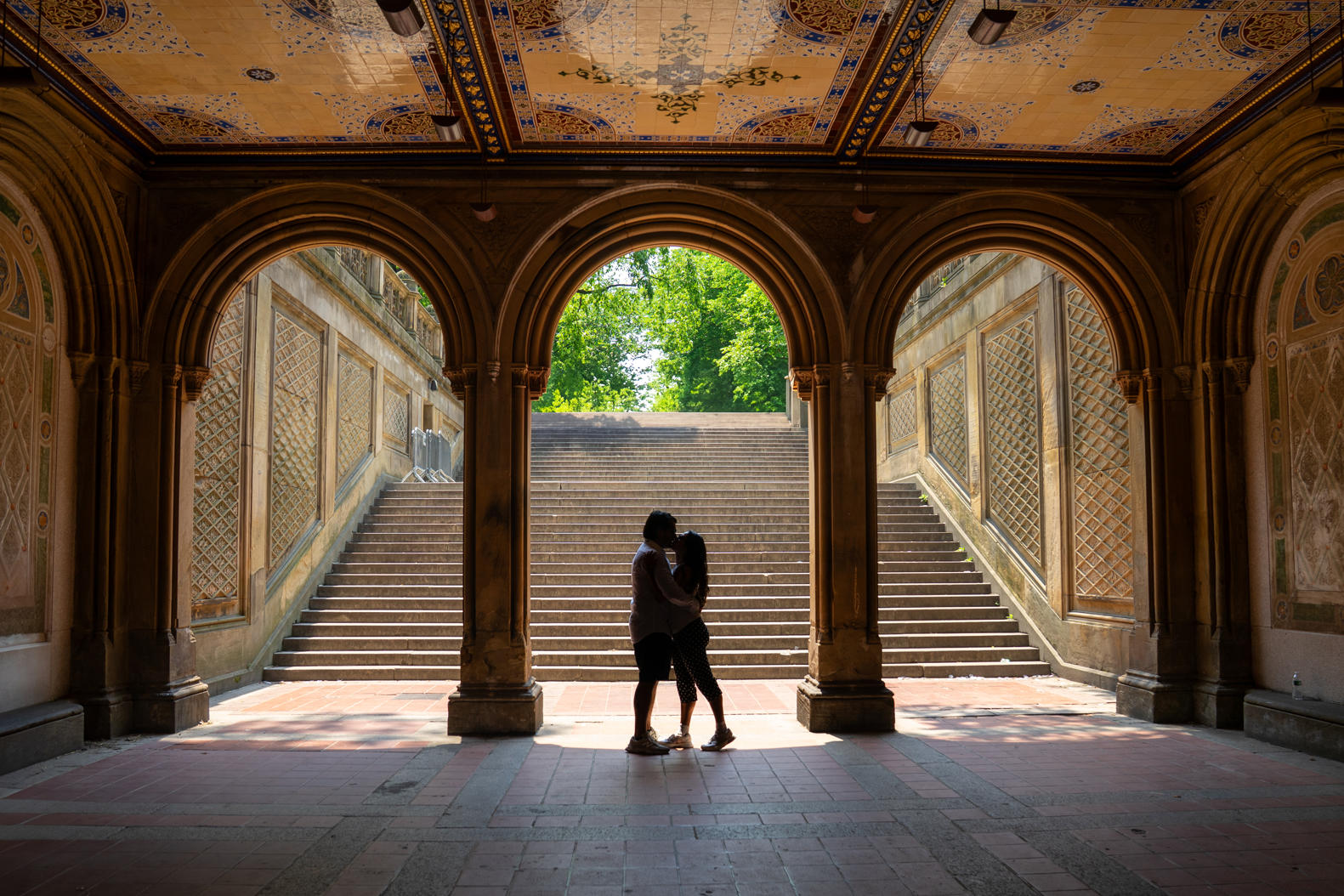 Couple embracing under the arches of a stone terrace at the foot of a grand staircase