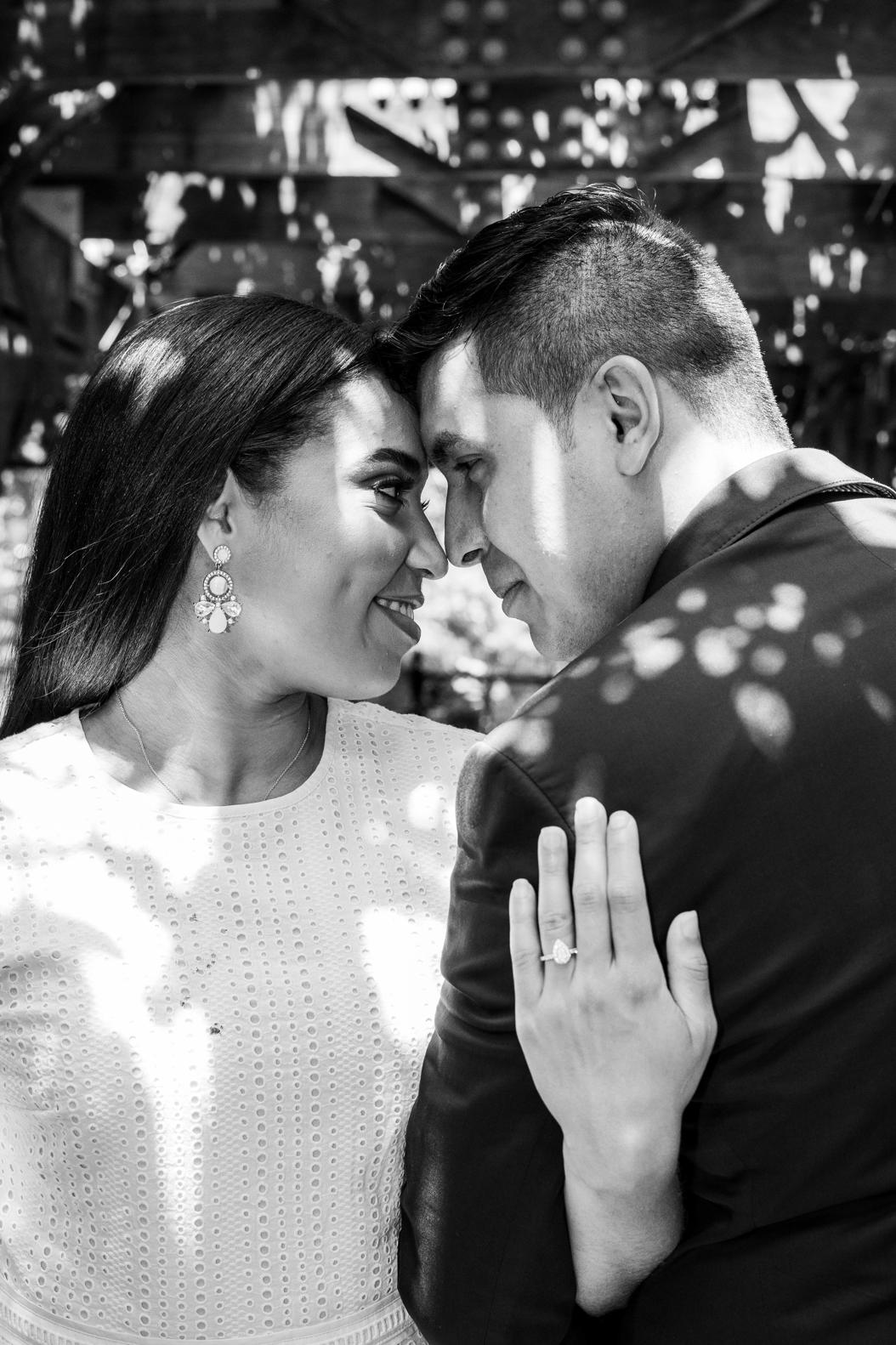 Black and white portrait of a couple forehead to forehead, engagement ring in view