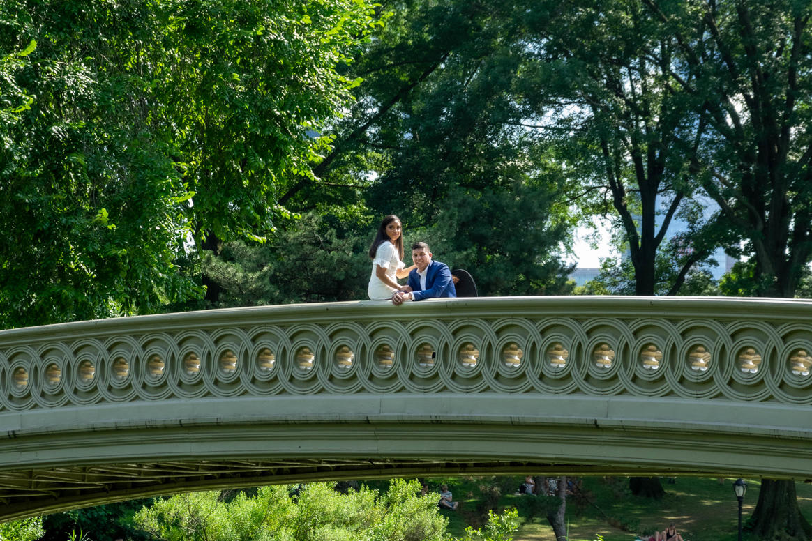 Couple together on an ornate white footbridge framed by summer trees
