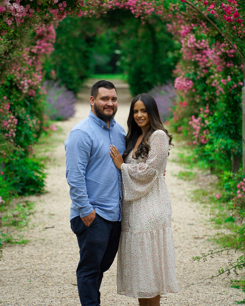 Couple pausing together under an archway of pink roses