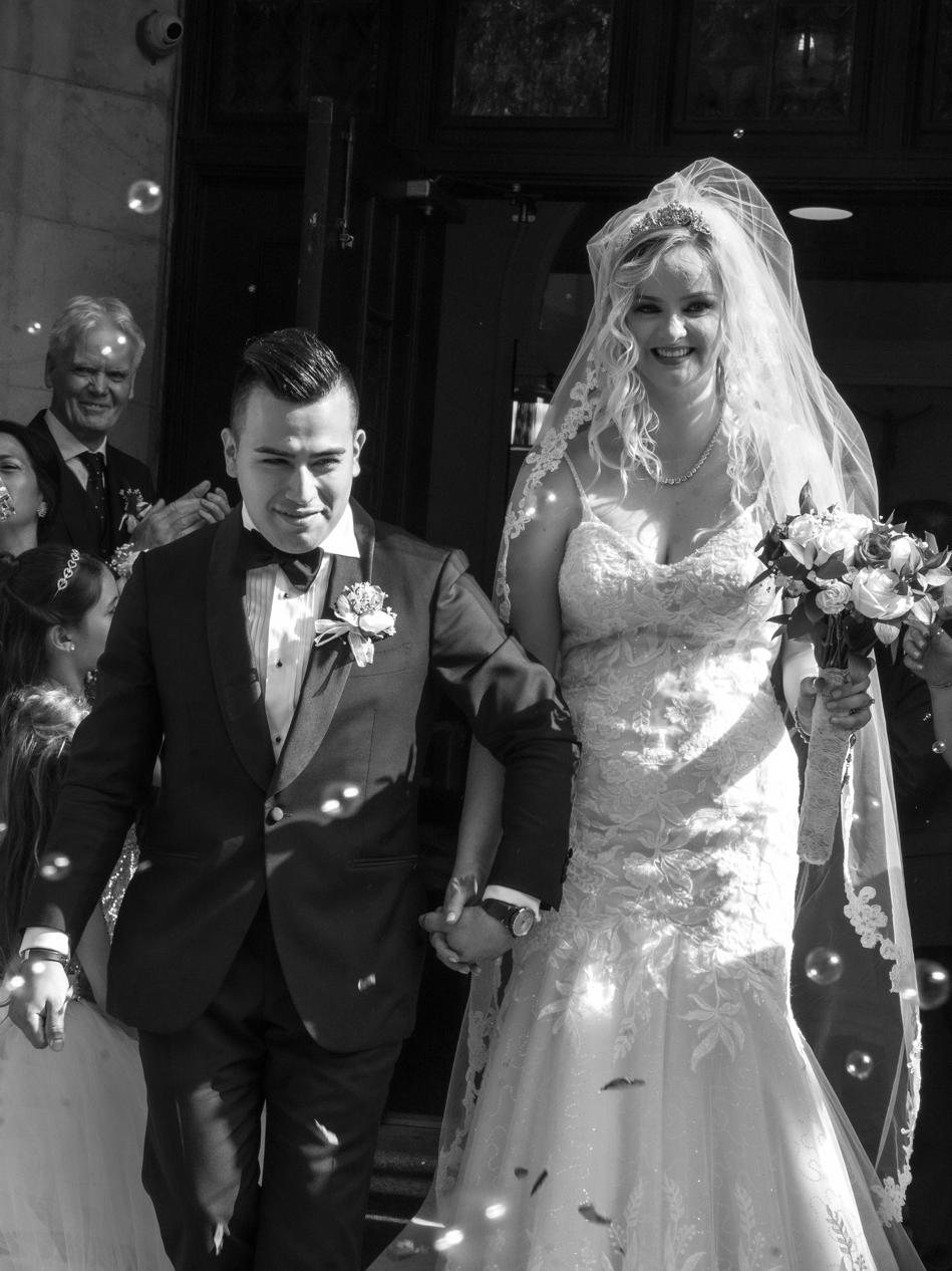 Newlyweds walking hand in hand out of the church through a cloud of bubbles