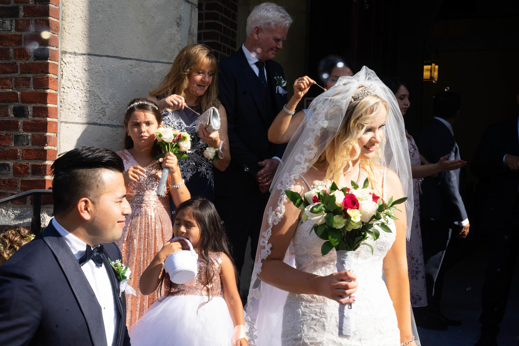 Bride holding her bouquet on the church steps as family sends her off with bubbles