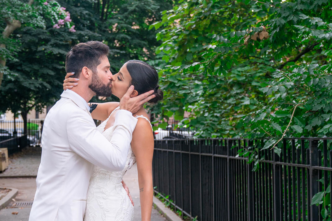 Couple sharing a kiss along a tree-lined park path after the ceremony