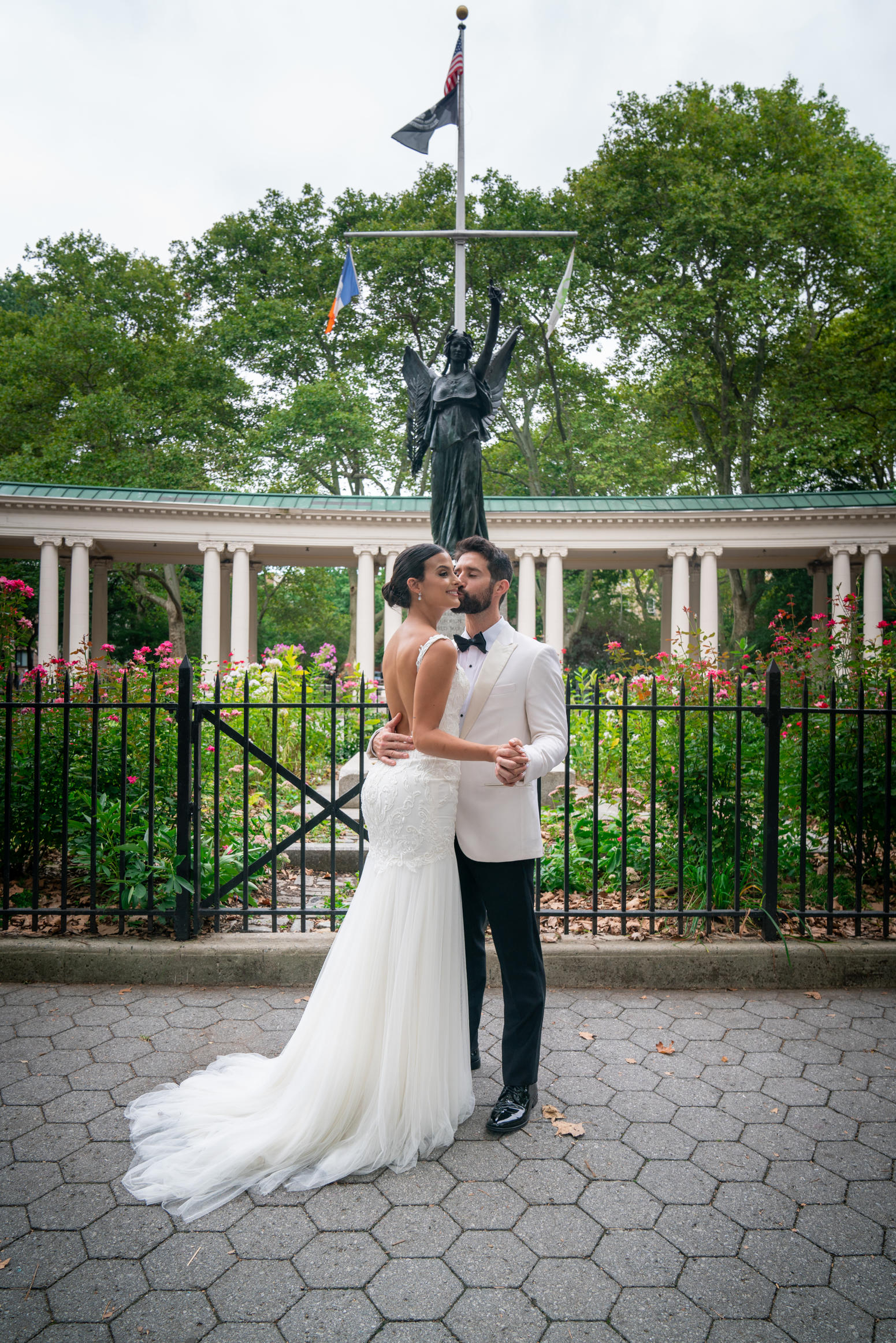 Bride and groom in a first dance pose in front of a park colonnade and rose garden