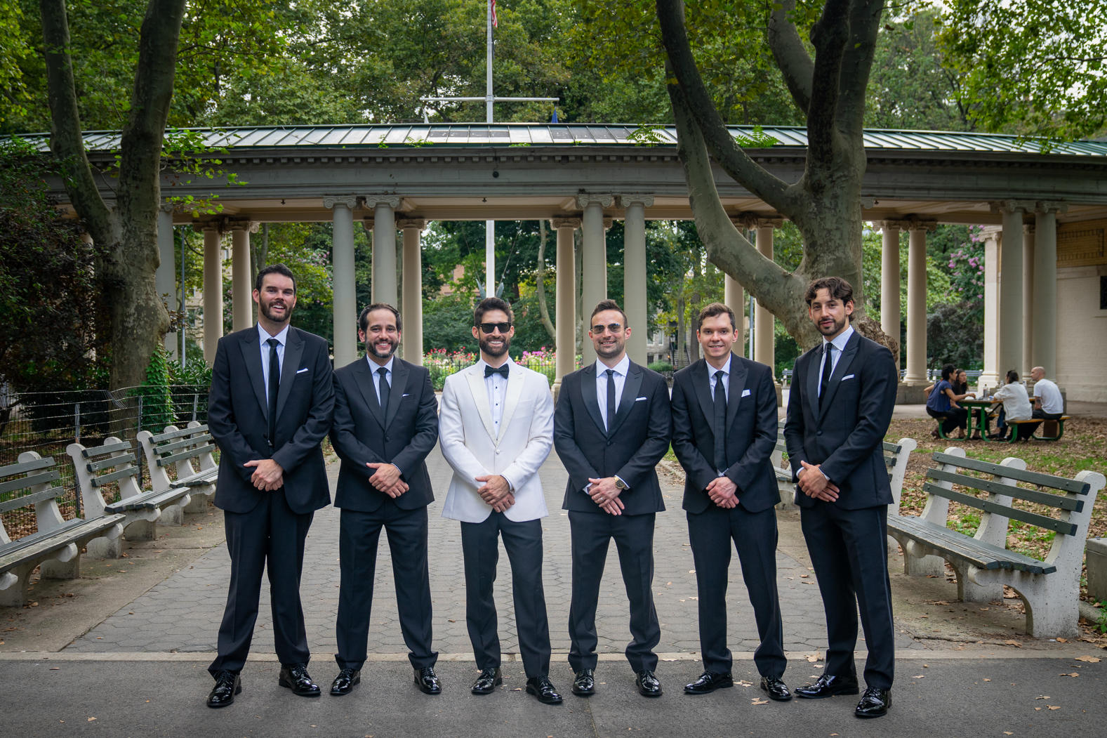 Groom in a white dinner jacket lined up with his groomsmen in the park