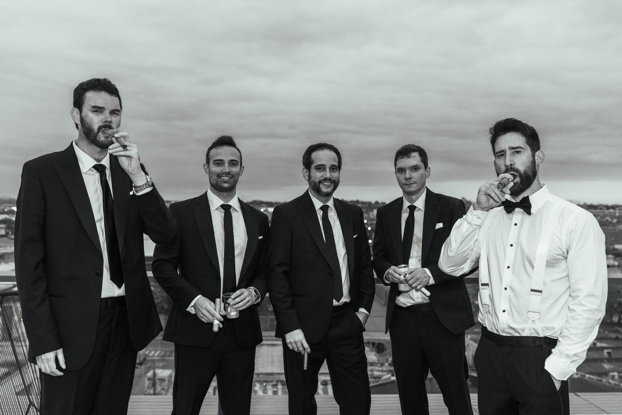 Groom and his groomsmen with cigars on the rooftop at dusk